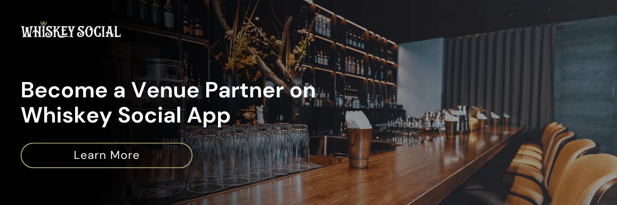 Image CTA for Whiskey Social with text ‘Become a Venue Partner on Whiskey Social App’ overlaid on an image of a modern whiskey bar, featuring a wooden counter lined with glassware and bar stools, with a Learn More button.